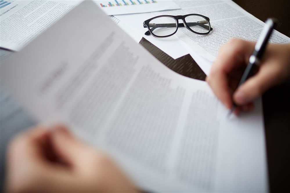 Person signing a blurred document with a pen.